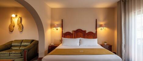 A hotel room with a large bed, a green armchair, a wooden headboard, and two wall-mounted lamps.