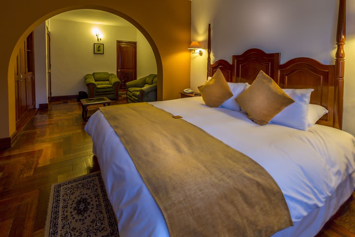 A hotel room with a large bed, a wooden headboard, a nightstand, and a green armchair.
