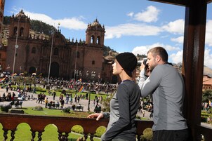 Un edificio histórico con cúpulas y torres de campanas, rodeado de una plaza pública con gente y banderas.