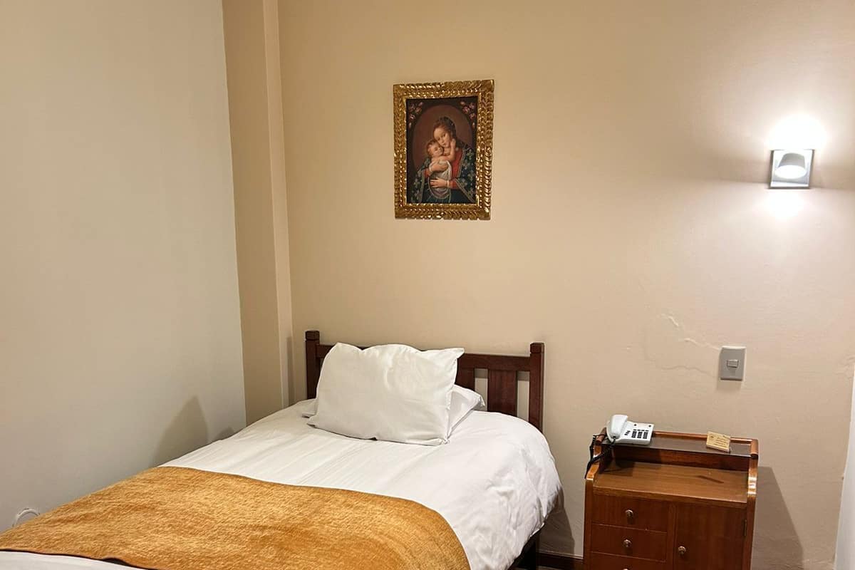 A bedroom with a wooden bed, a nightstand with a telephone, and a wall-mounted light.
