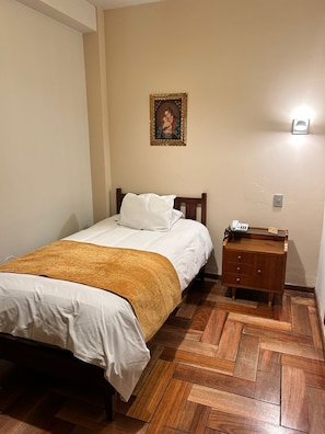 A bedroom with a wooden bed, a nightstand with a telephone, and a wall-mounted light. - El Virrey by Katari  (Cusco)