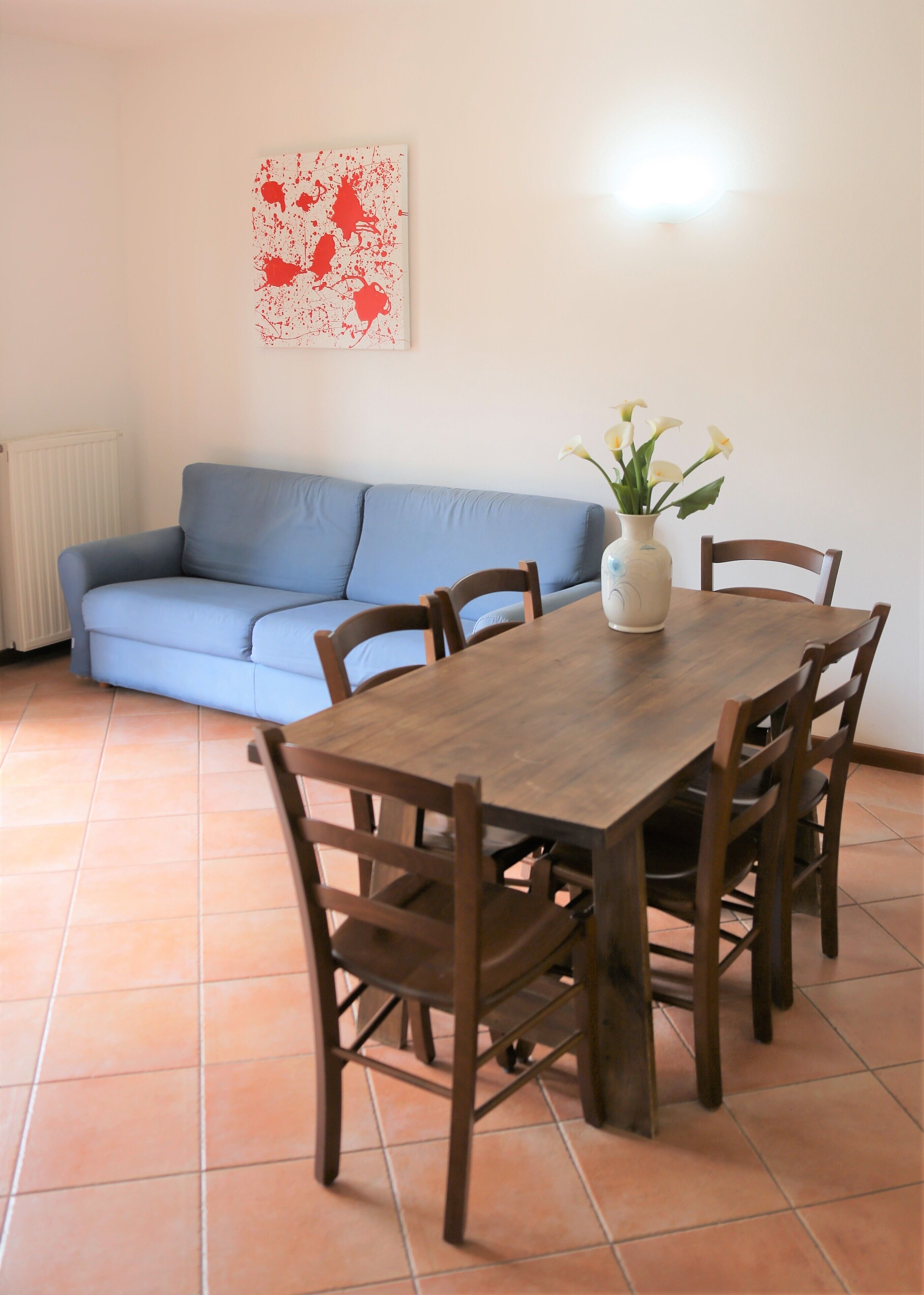 A dining area with a wooden table and chairs, a blue sofa, and a vase with flowers.