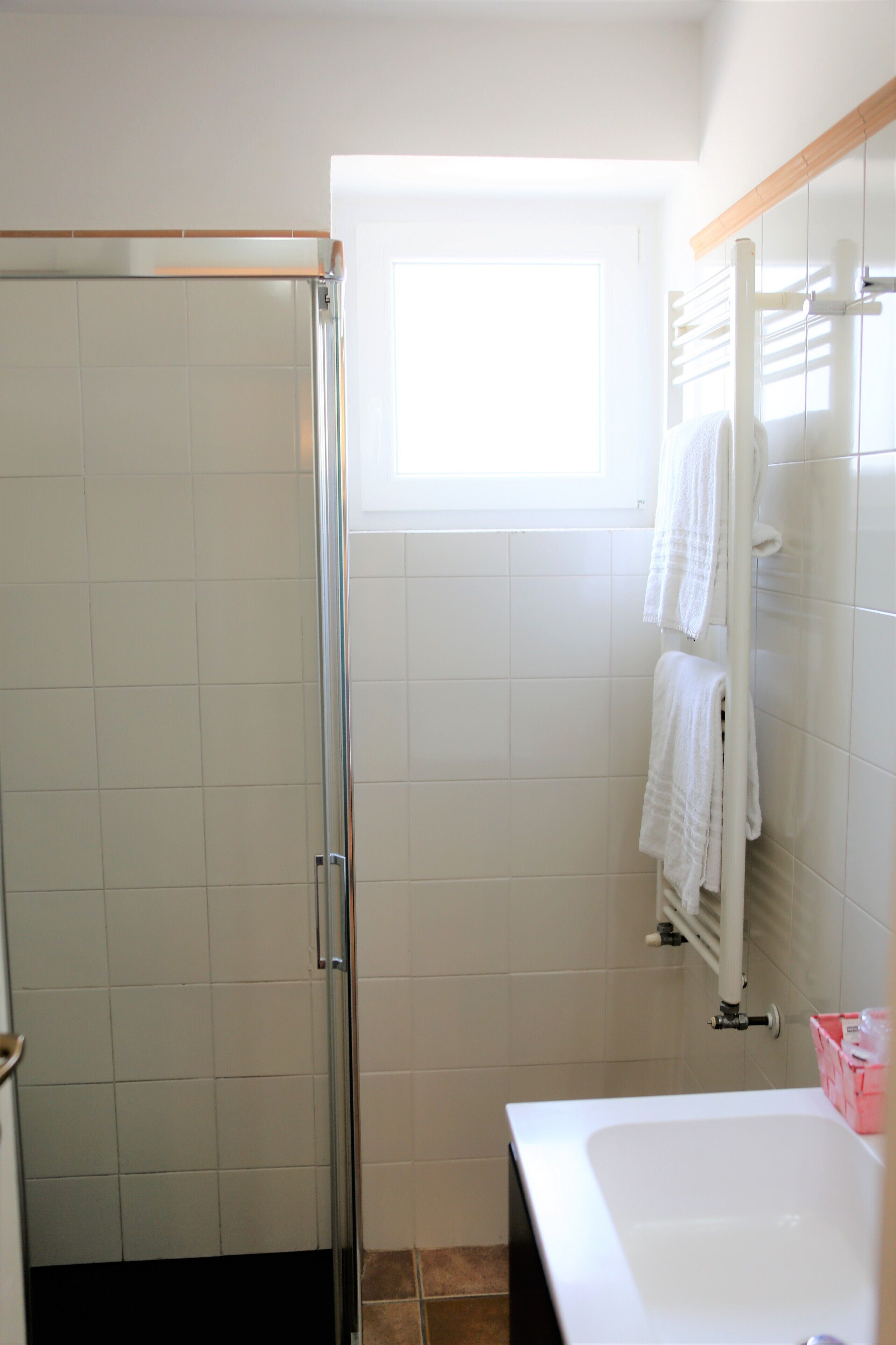 A bathroom with a glass shower enclosure, a white bathtub, and a window providing natural light.