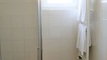 A bathroom with a glass shower enclosure, a white bathtub, and a window providing natural light.