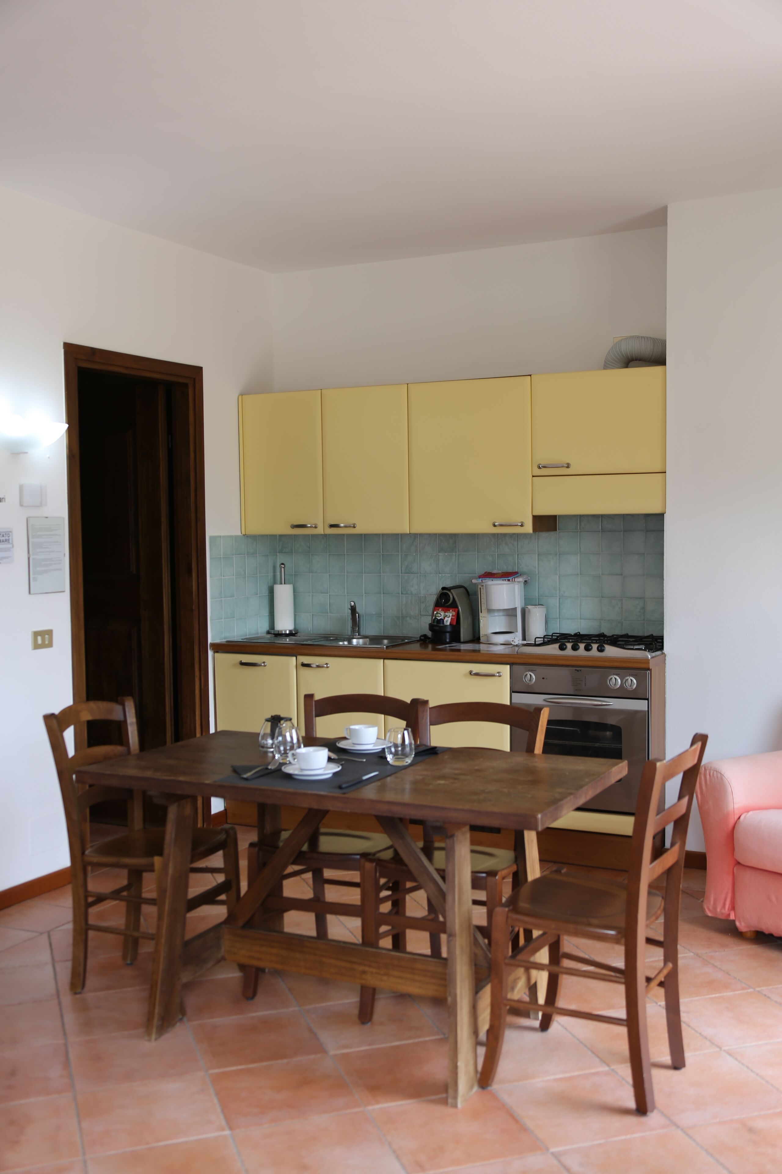 A compact kitchen with yellow cabinets, a dining table with chairs, and a pink sofa in the corner.