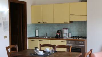 A compact kitchen with yellow cabinets, a dining table with chairs, and a pink sofa in the corner.