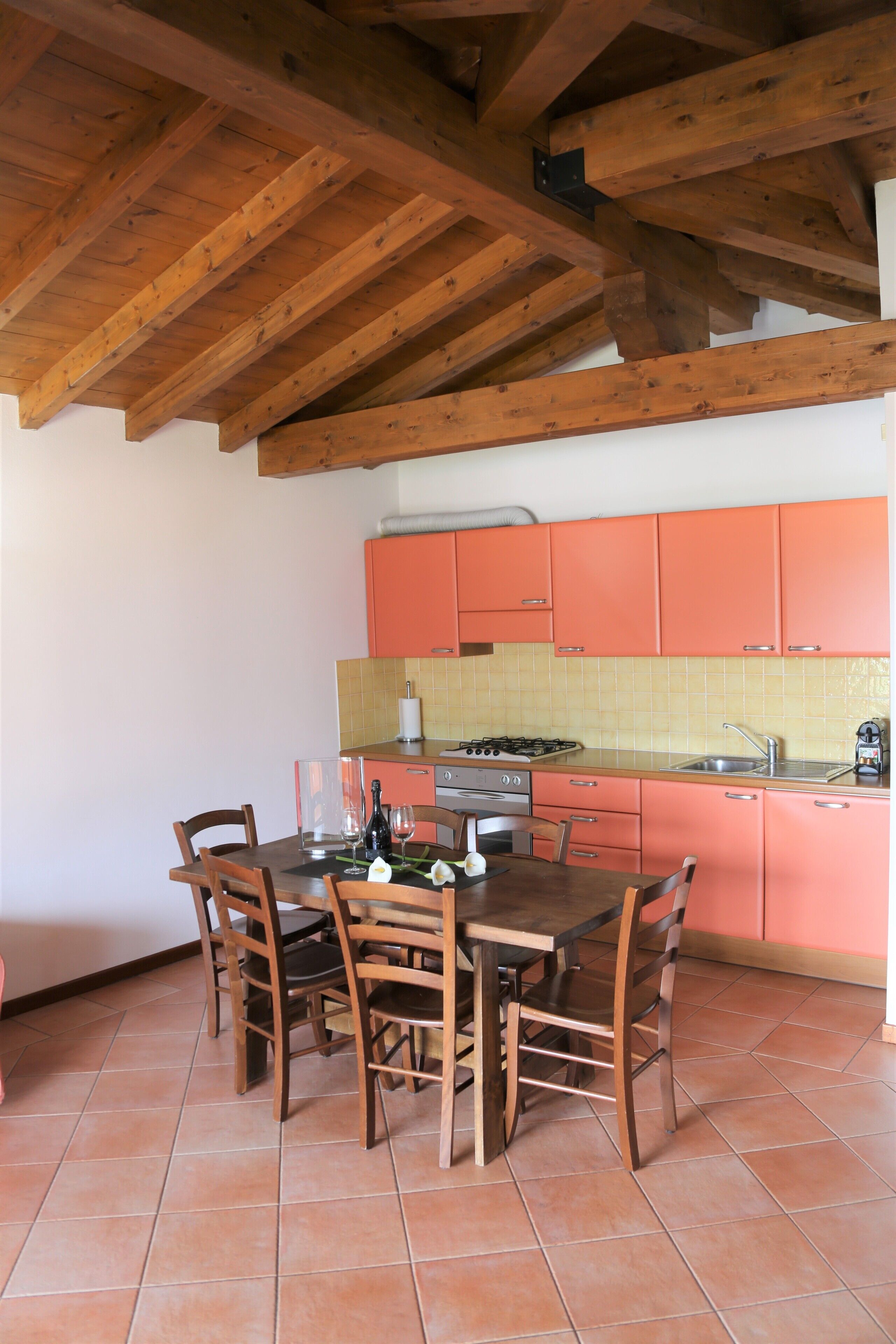 Une cuisine avec des poutres en bois, une table à manger avec des chaises et des meubles de rangement orange.