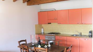 Une cuisine avec des poutres en bois, une table à manger avec des chaises et des meubles de rangement orange.