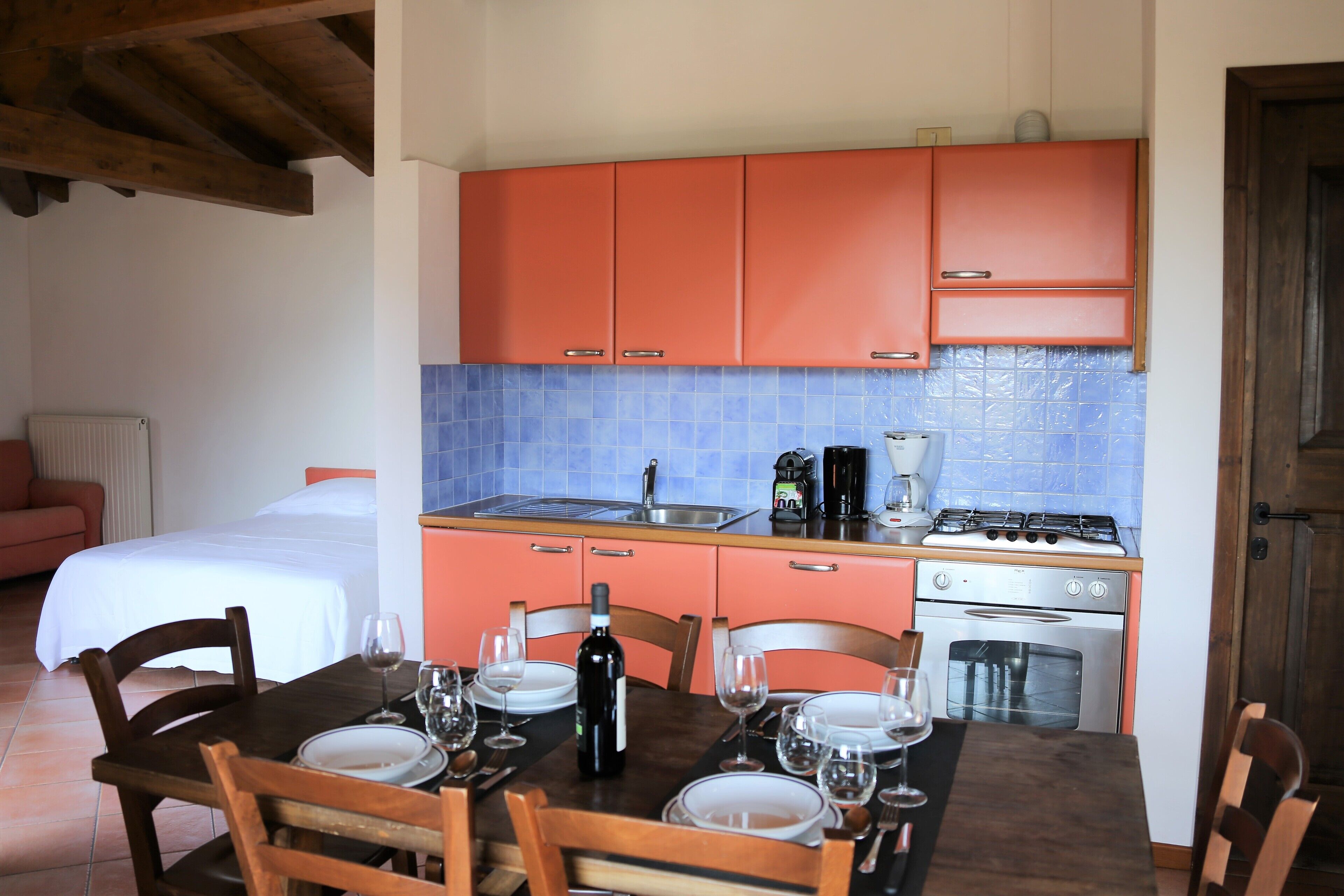 Una cocina compacta con armarios naranjas, una estufa y un lavamanos. Hay una mesa de comedor con platos y copas de vino.