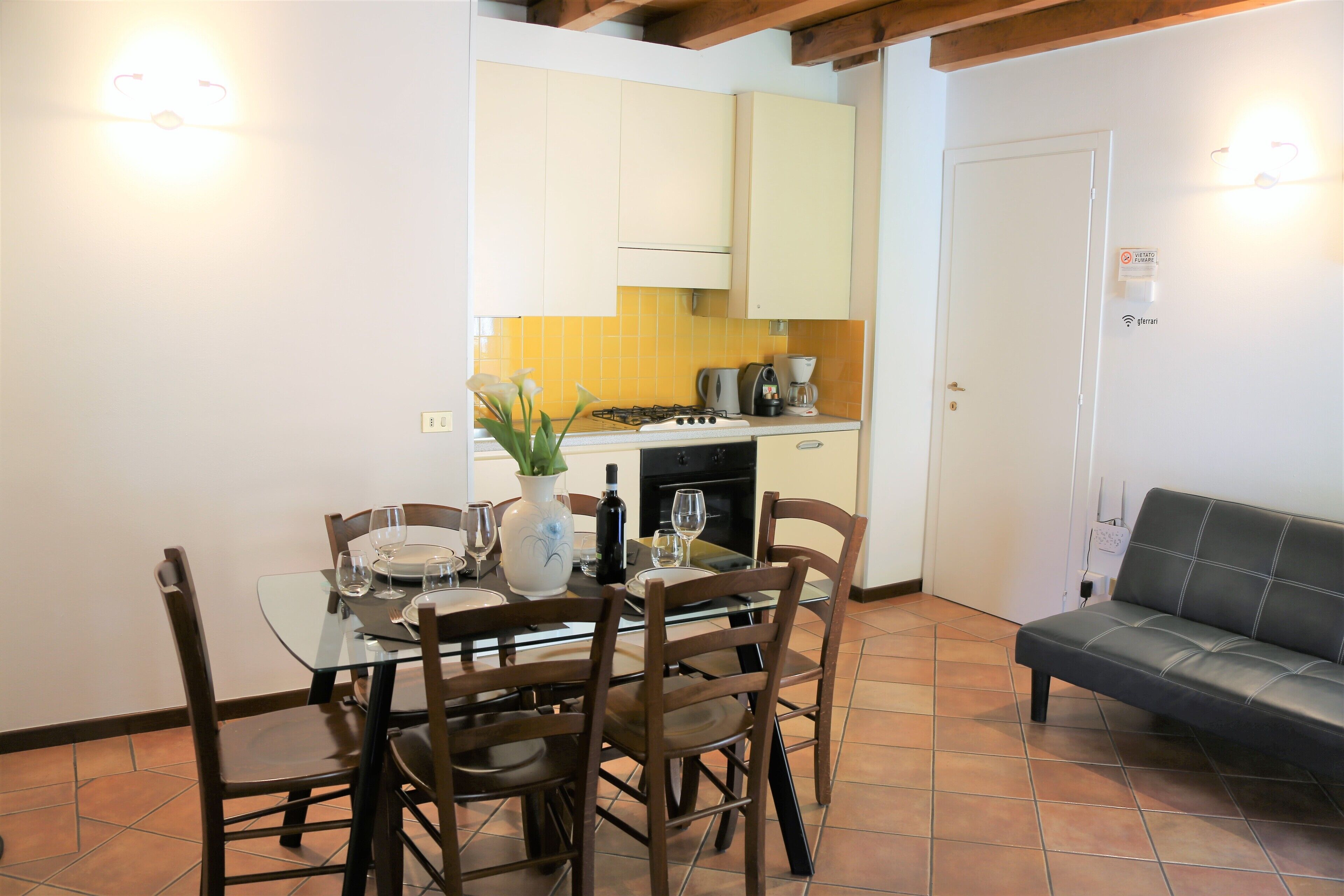 A dining area with a glass table, wooden chairs, and a sofa.
