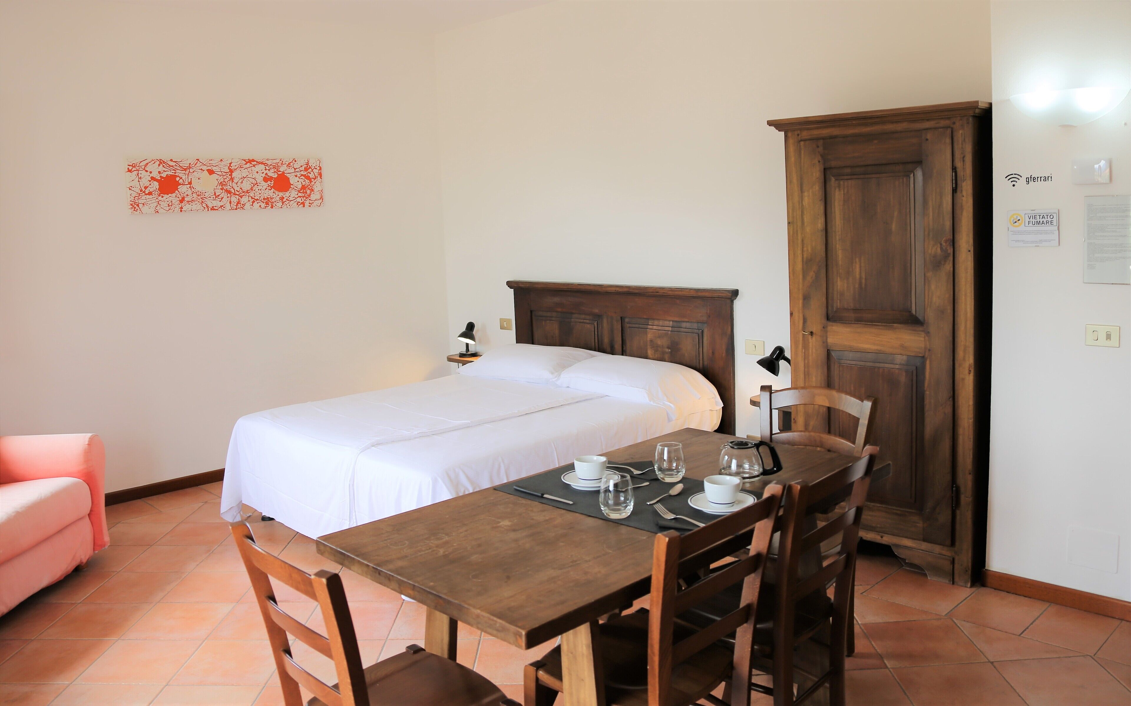 Ein Schlafzimmer mit einem Bett, einem Holztisch mit Stühlen, einem rosa Sessel und einem Holzschrank.