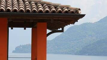 A building with a tiled roof and orange walls, overlooking a body of water and hills.