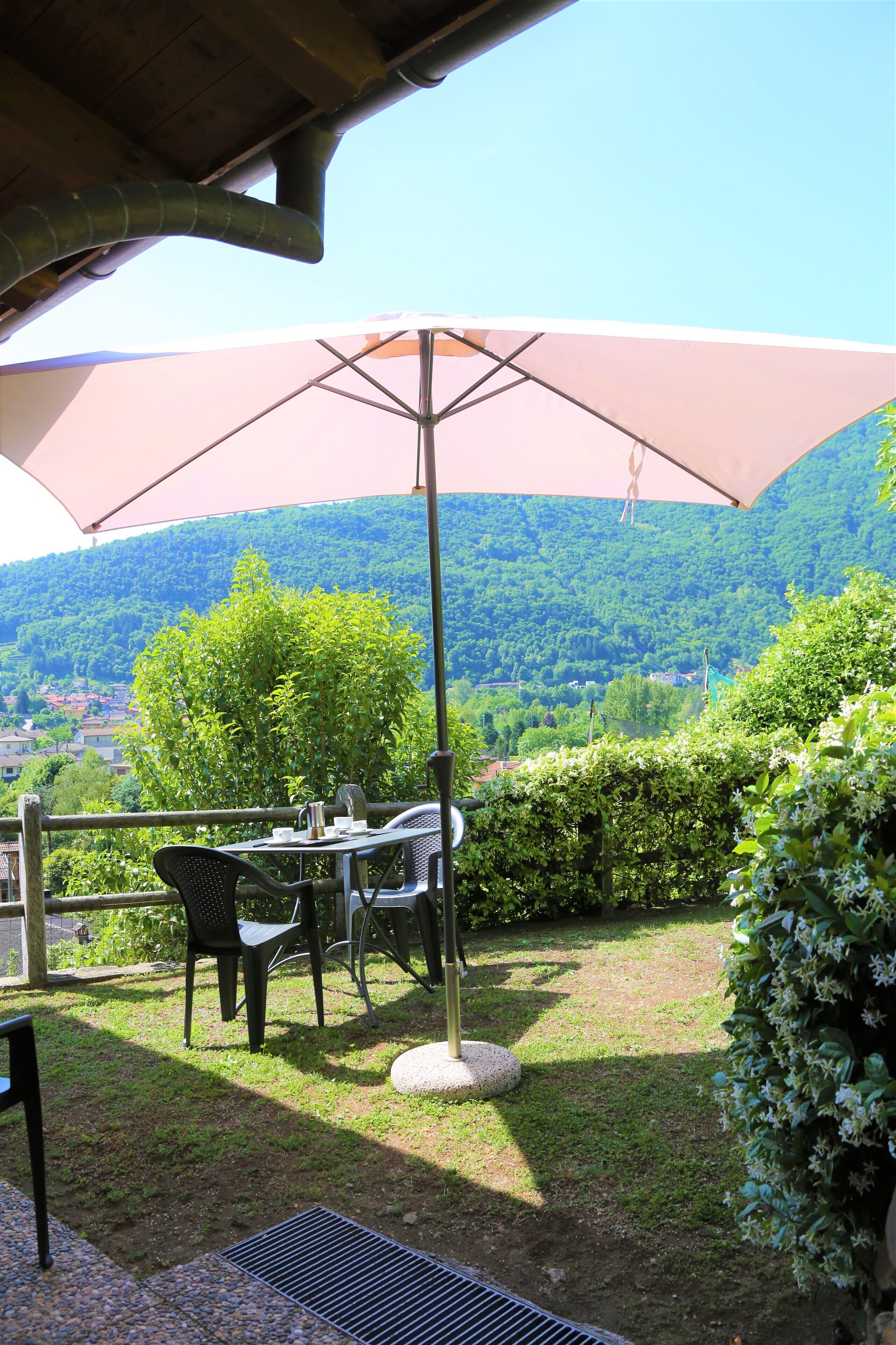 An outdoor patio with a table and chairs under a large umbrella, overlooking a lush valley.