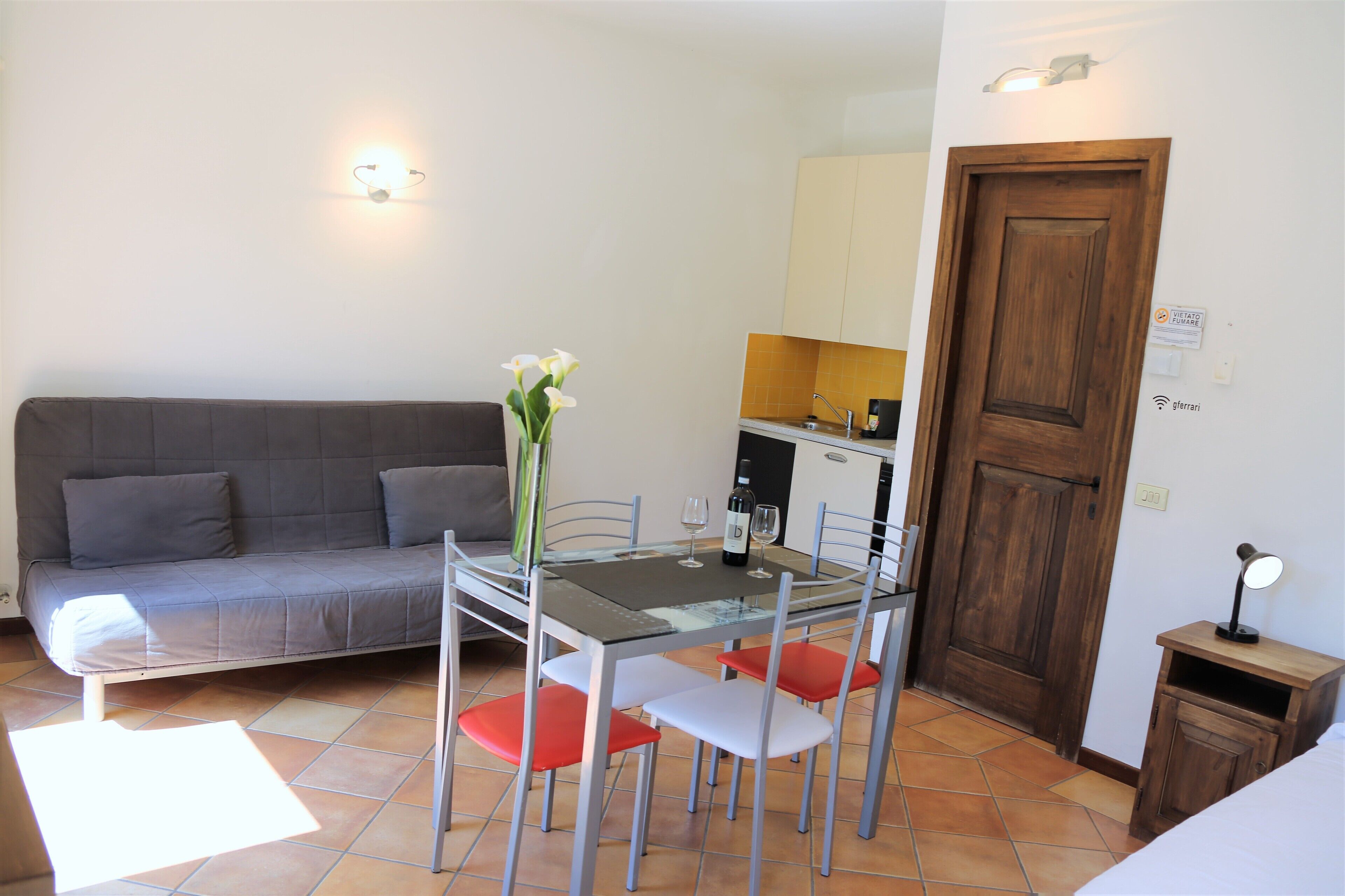A compact living space with a sofa, a dining table with chairs, a small kitchen area, and a wooden door.