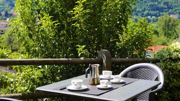 Una mesa al aire libre con tazas y una cafetera, rodeada de follaje y una valla de madera.