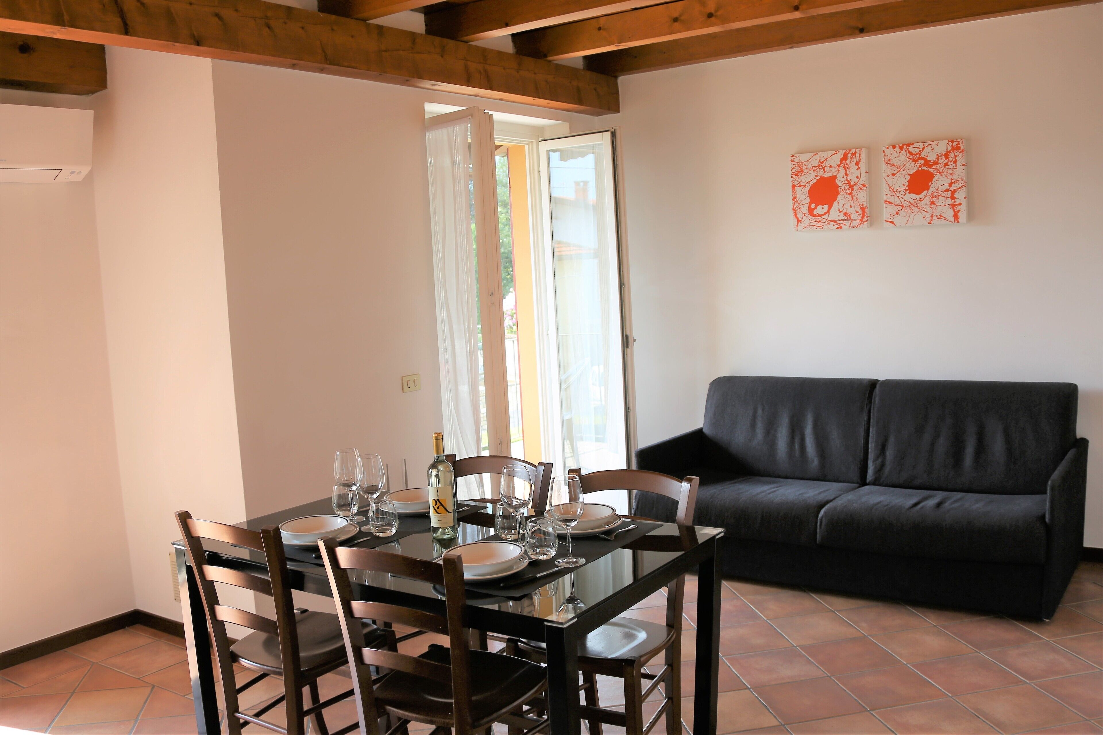A dining area with a table set for four, a black sofa, and two abstract paintings on the wall.