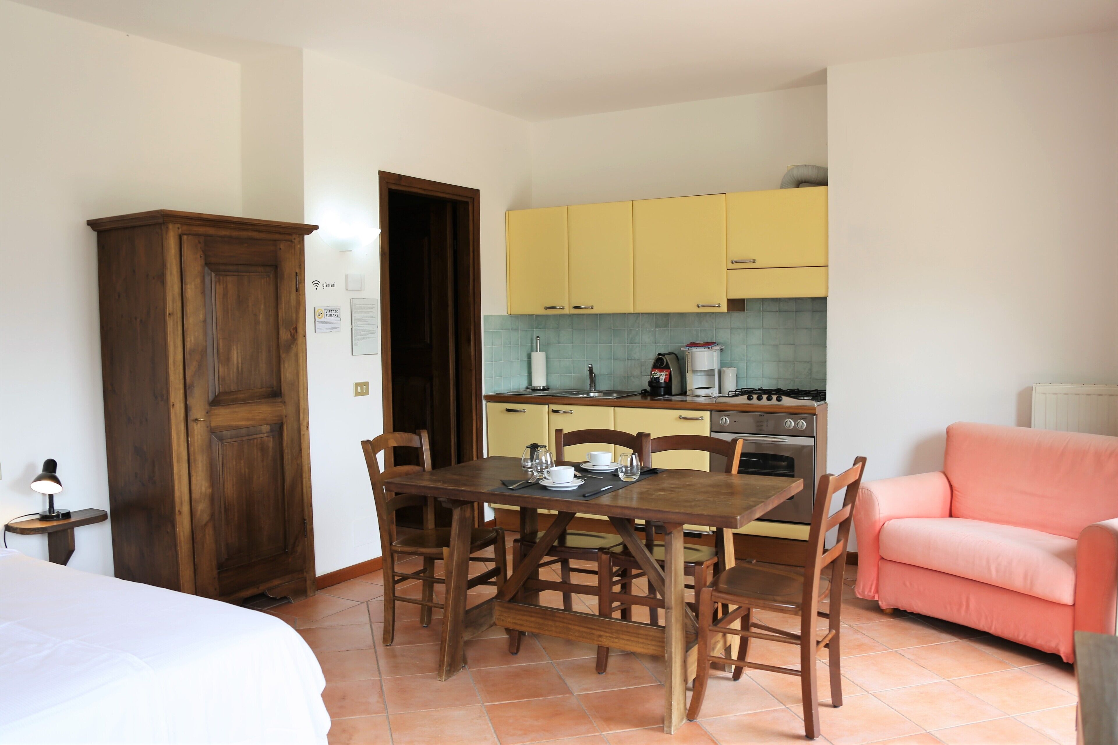 A compact kitchen with yellow cabinets, a dining table with chairs, a pink sofa, and a wooden wardrobe.