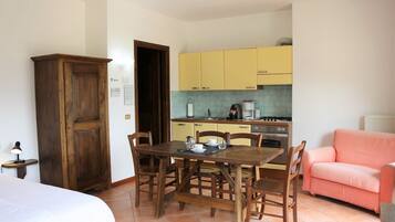 A compact kitchen with yellow cabinets, a dining table with chairs, a pink sofa, and a wooden wardrobe.