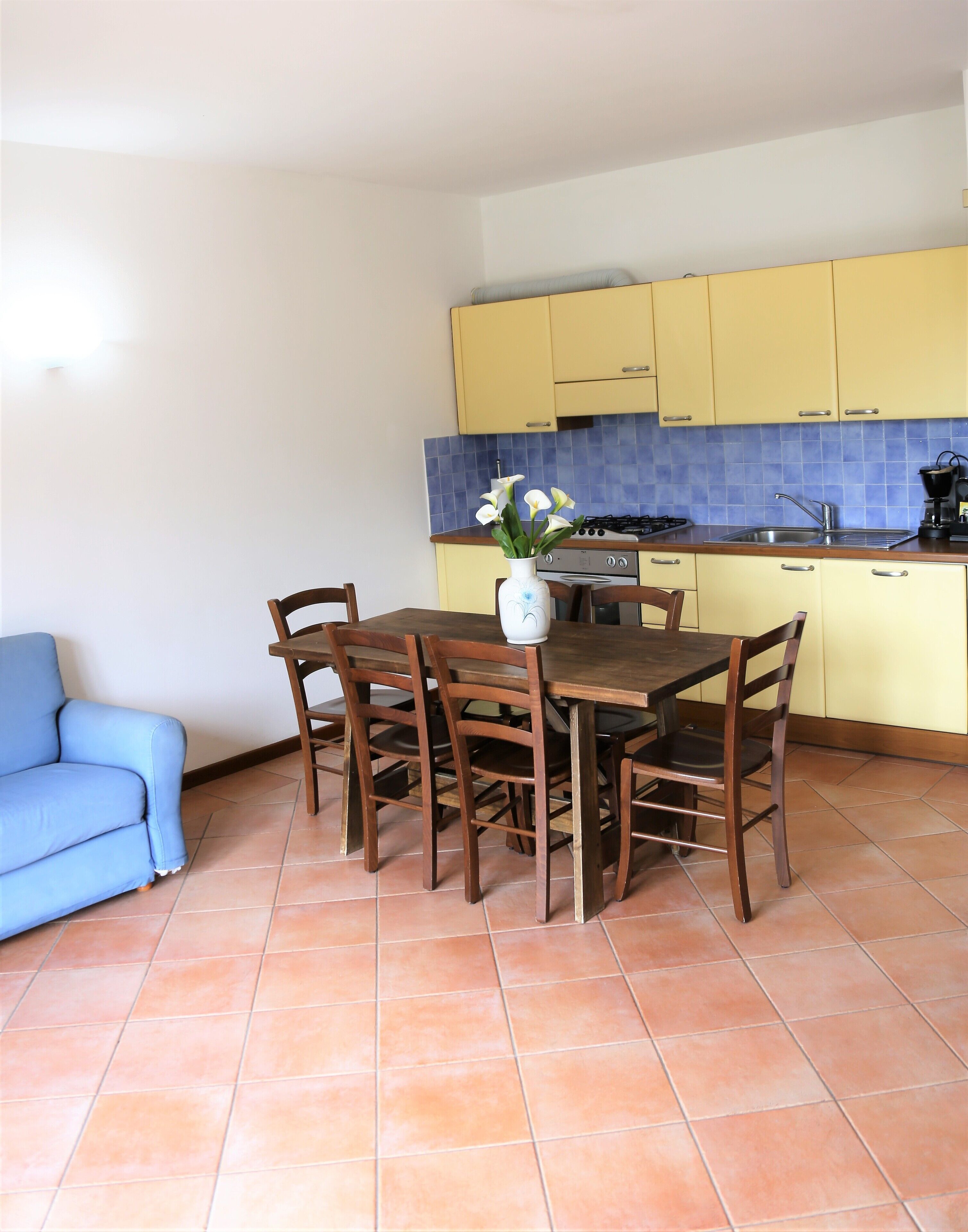 Ein Essbereich mit Holztisch und -stühlen, einer Blumenvase und einem blauen Sofa.