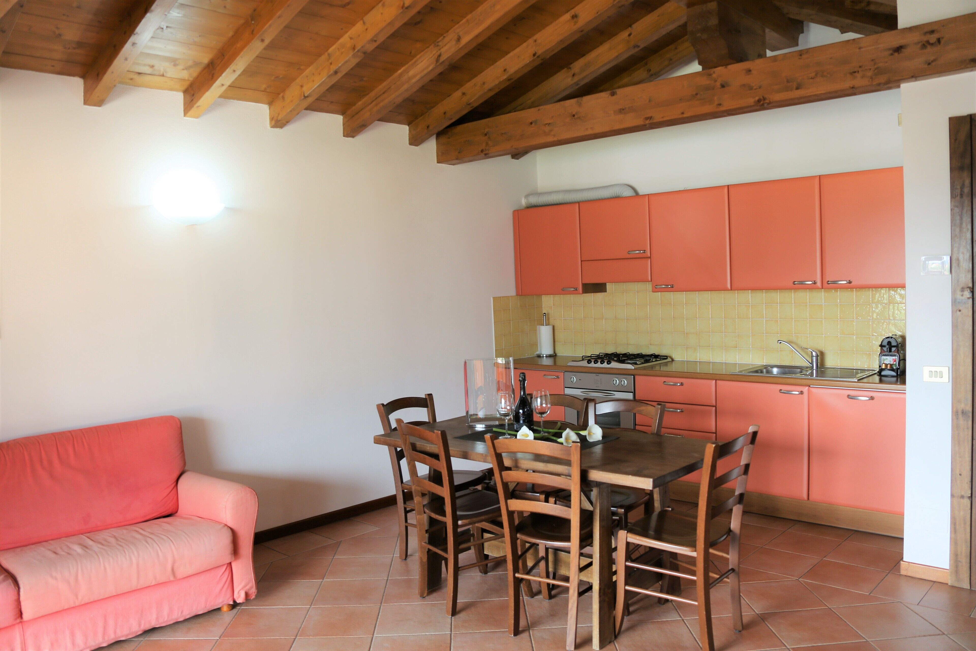 Una cocina con armarios de madera, una mesa de comedor con sillas y un sofá rosa.