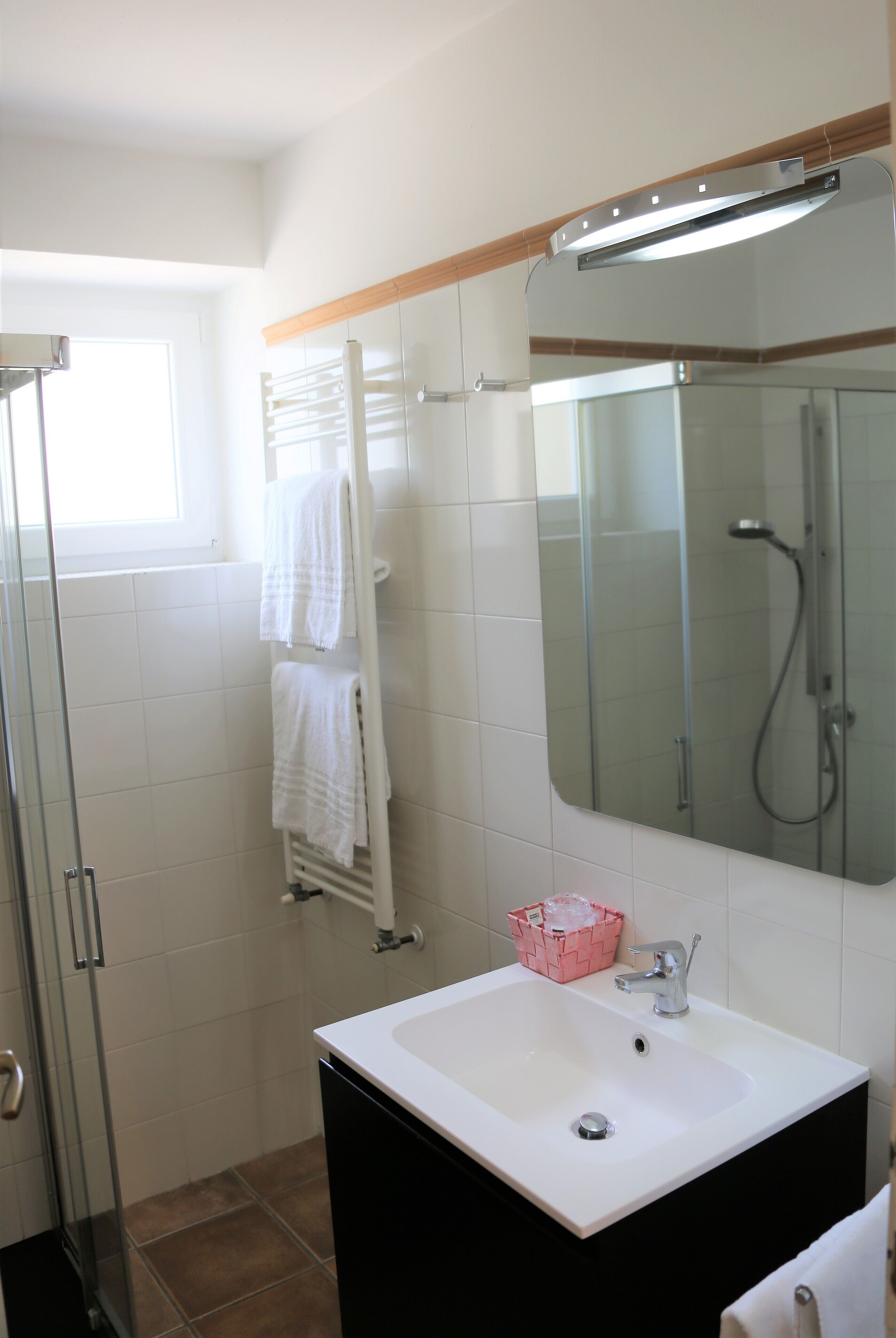 Un baño con un lavamanos blanco, cabina de ducha con mampara de vidrio y un espejo sobre el lavamanos.
