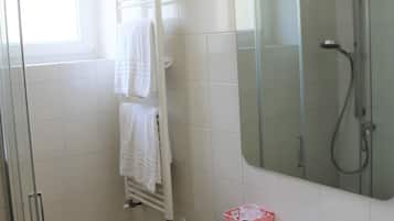 Un baño con un lavamanos blanco, cabina de ducha con mampara de vidrio y un espejo sobre el lavamanos.