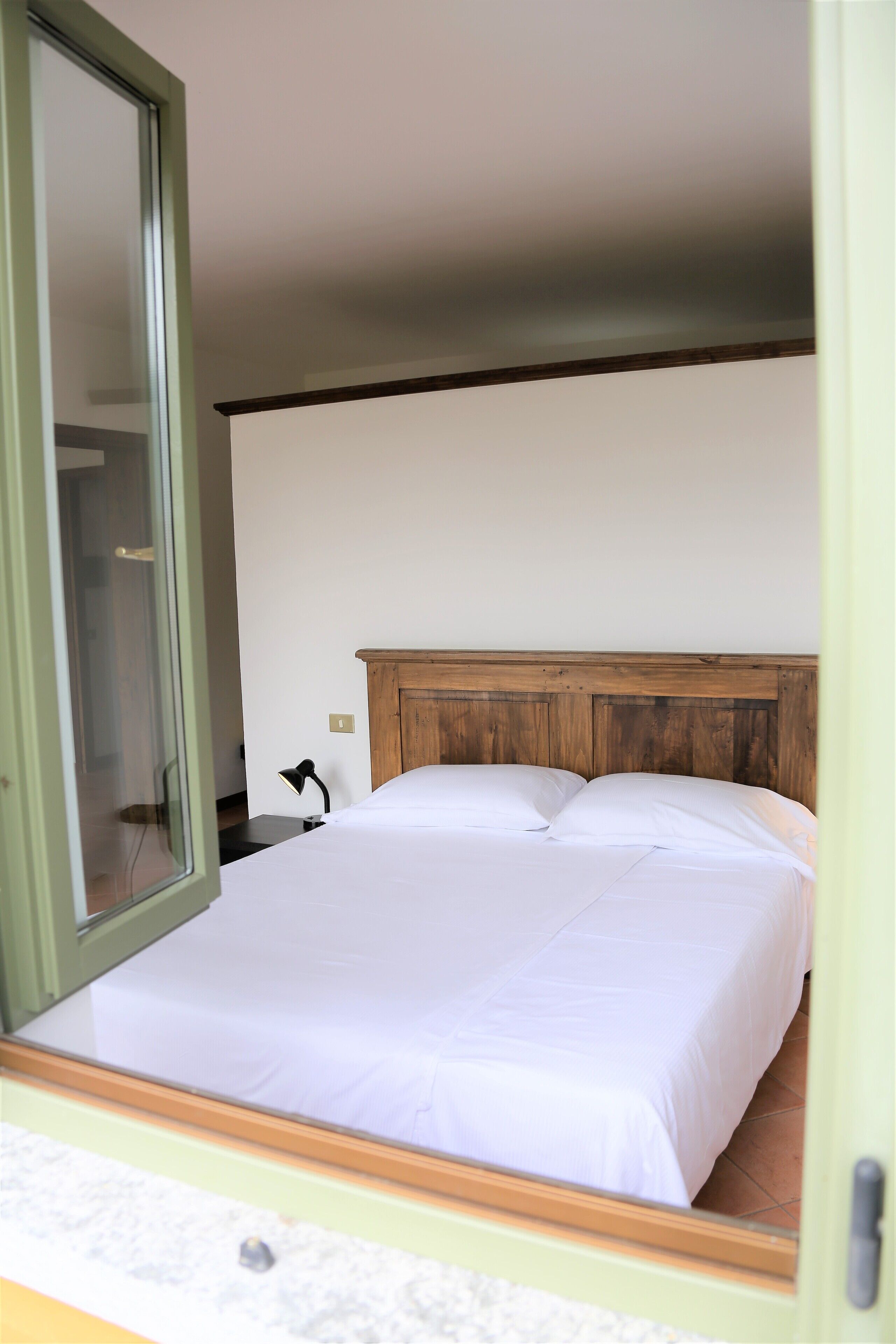 A bedroom with a wooden headboard, a bed with white bedding, a nightstand with a lamp, and a sliding glass door leading to a bathroom.