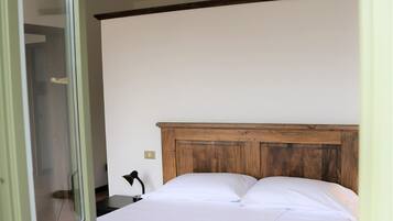 A bedroom with a wooden headboard, a bed with white bedding, a nightstand with a lamp, and a sliding glass door leading to a bathroom.