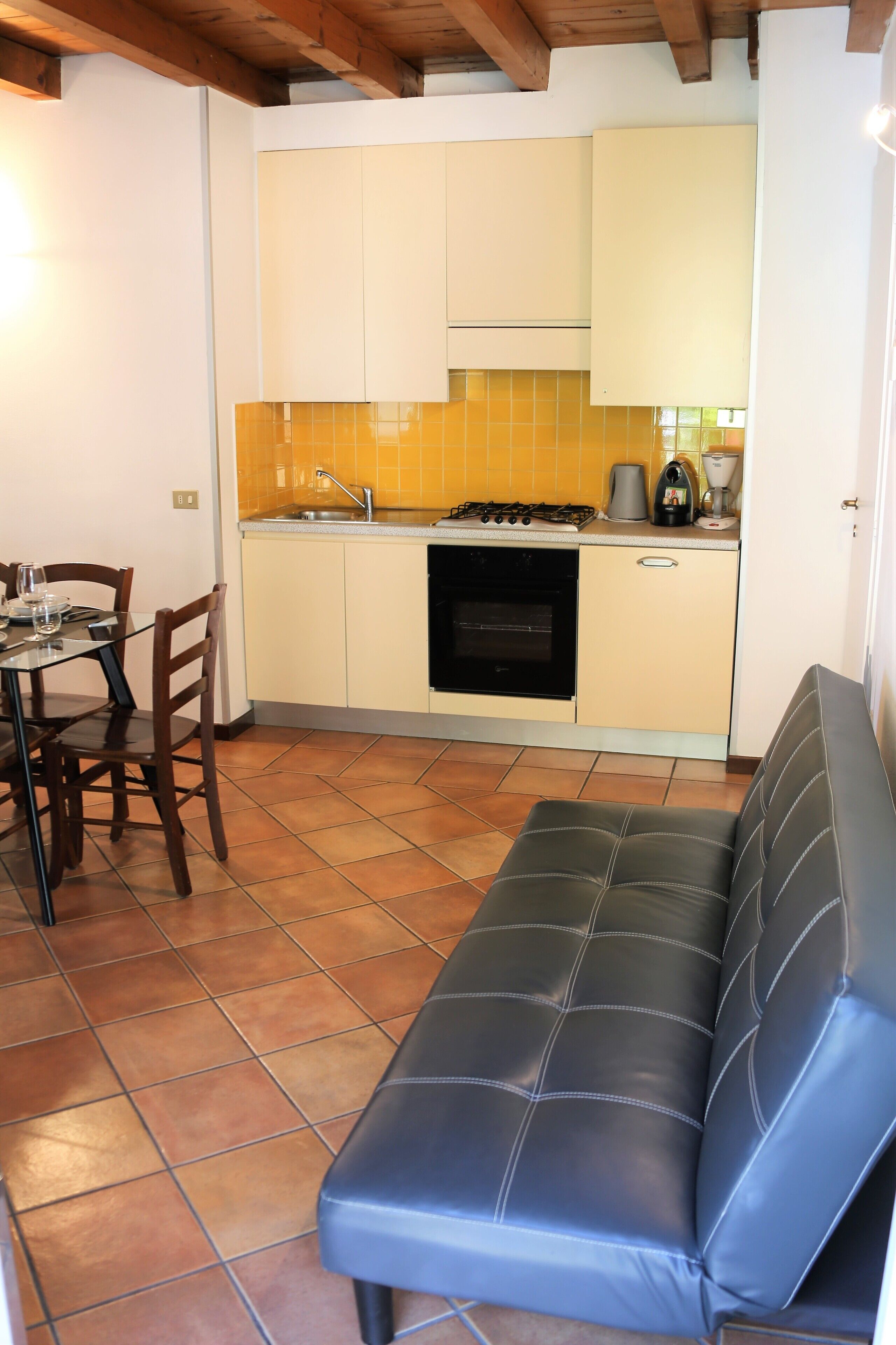 A compact kitchen with a dining area, a sofa, and a tiled floor.