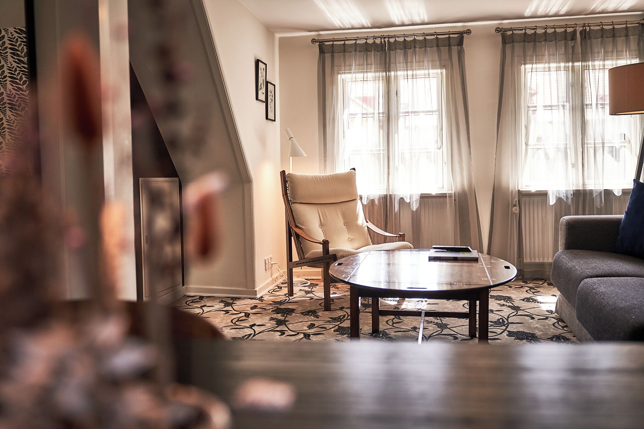 Una sala de estar con una mesa redonda, un sofá, una silla y una ventana con cortinas.