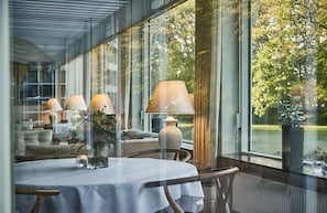 Comedor con una mesa preparada para dos, una lámpara y vistas al exterior con vegetación.