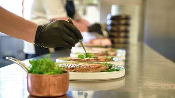 A chef preparing food, with plates of dishes and a copper pot on a stainless steel counter.