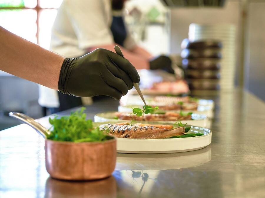 A chef preparing food, with plates of dishes and a copper pot on a stainless steel counter.