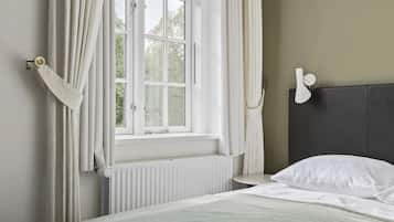 A bedroom with a bed, a window with curtains, a radiator, and a wall-mounted light fixture.