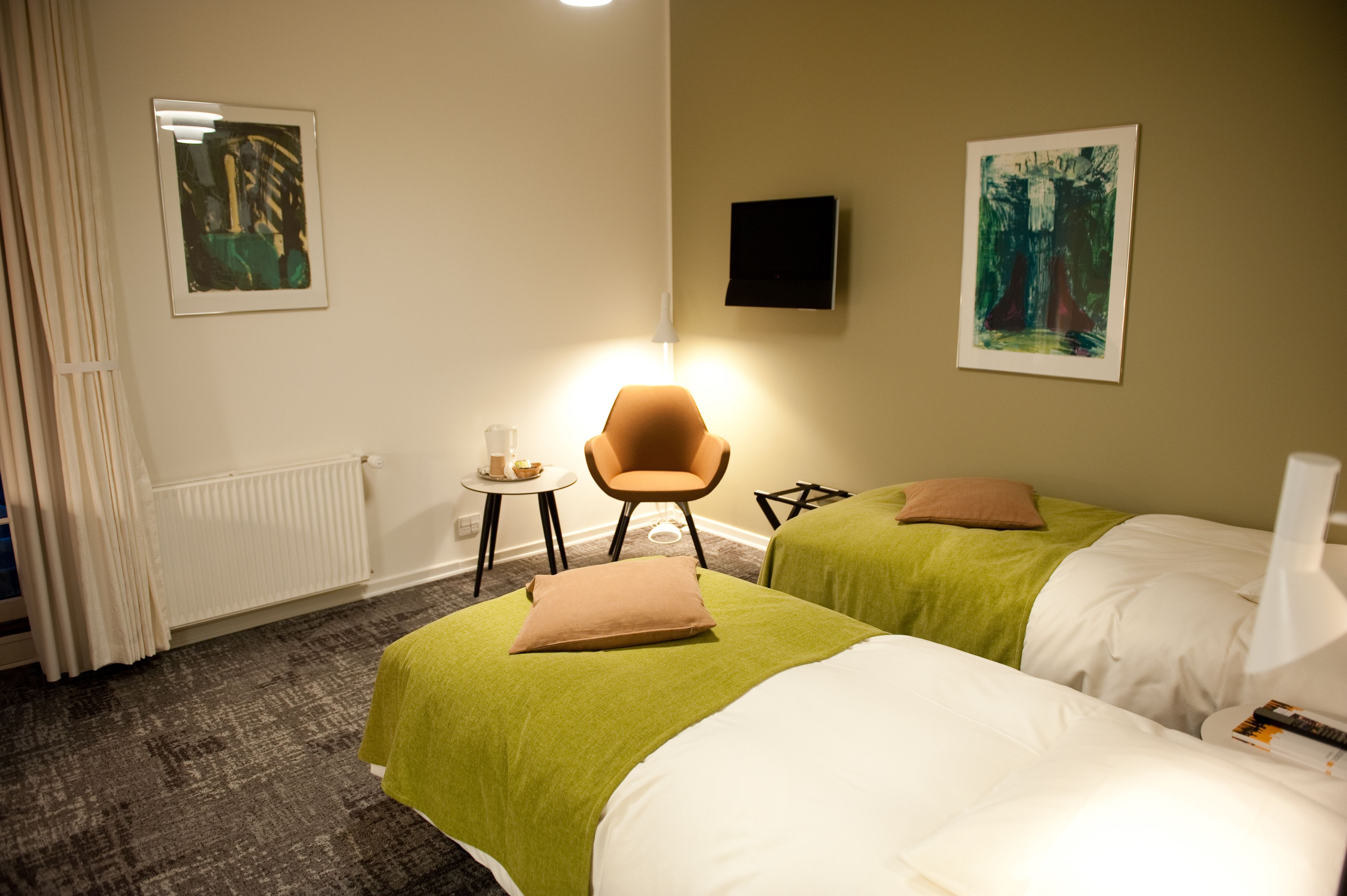 Een hotelkamer met twee bedden, een stoel, een tafeltje en kunstwerken aan de muur.