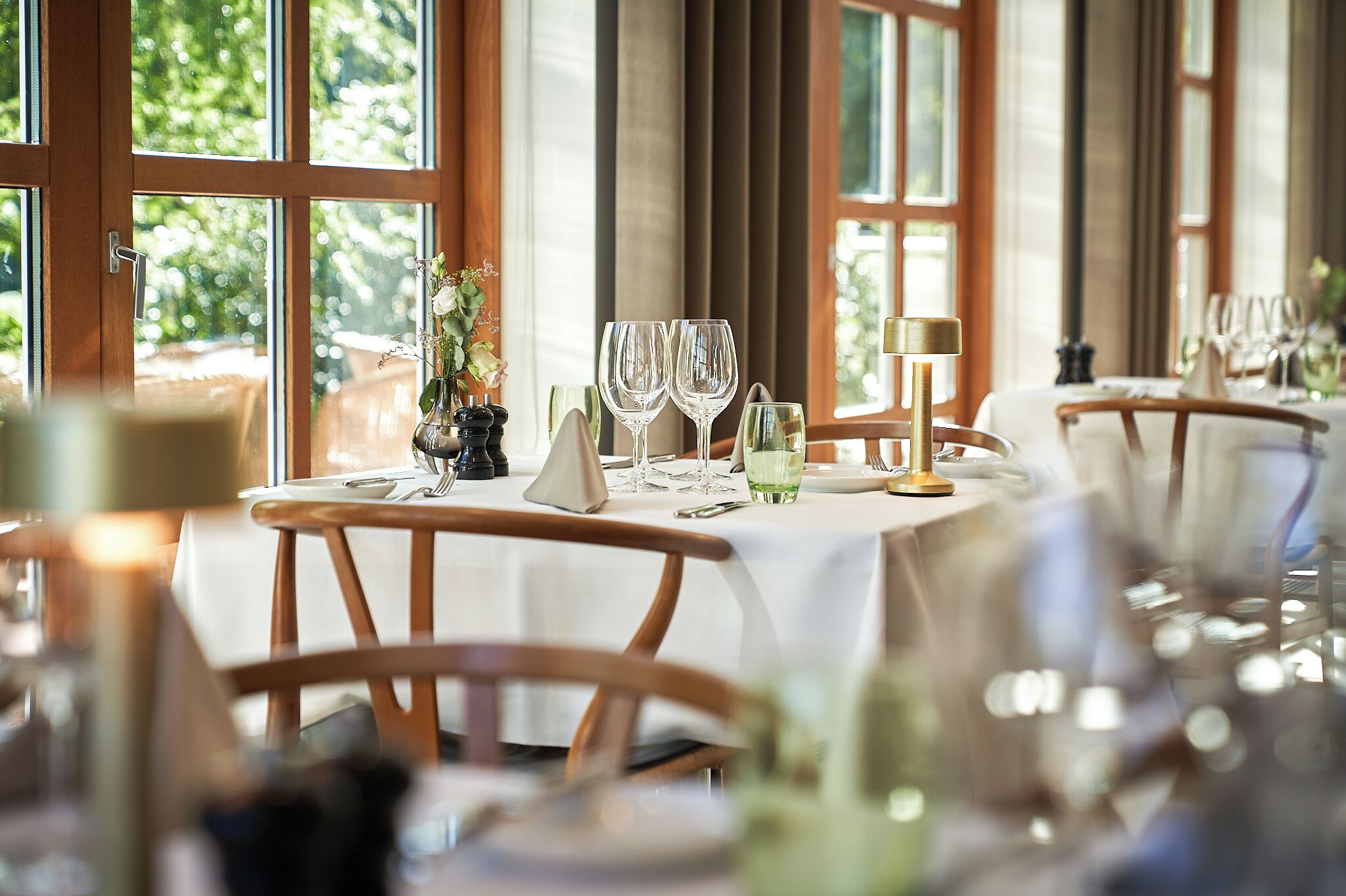 A dining area with wooden chairs, a white tablecloth, and a window with a view of greenery.