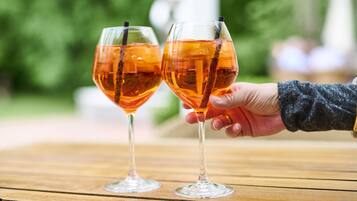 Deux verres contenant un liquide ambré sont posés sur une table en bois, avec un arrière-plan flou de couleur verte.