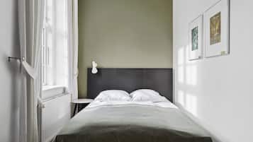 Minimalistinen hotellihuone, jossa on sänky, yöpöytä ja seinään kiinnitetty valaisin.
