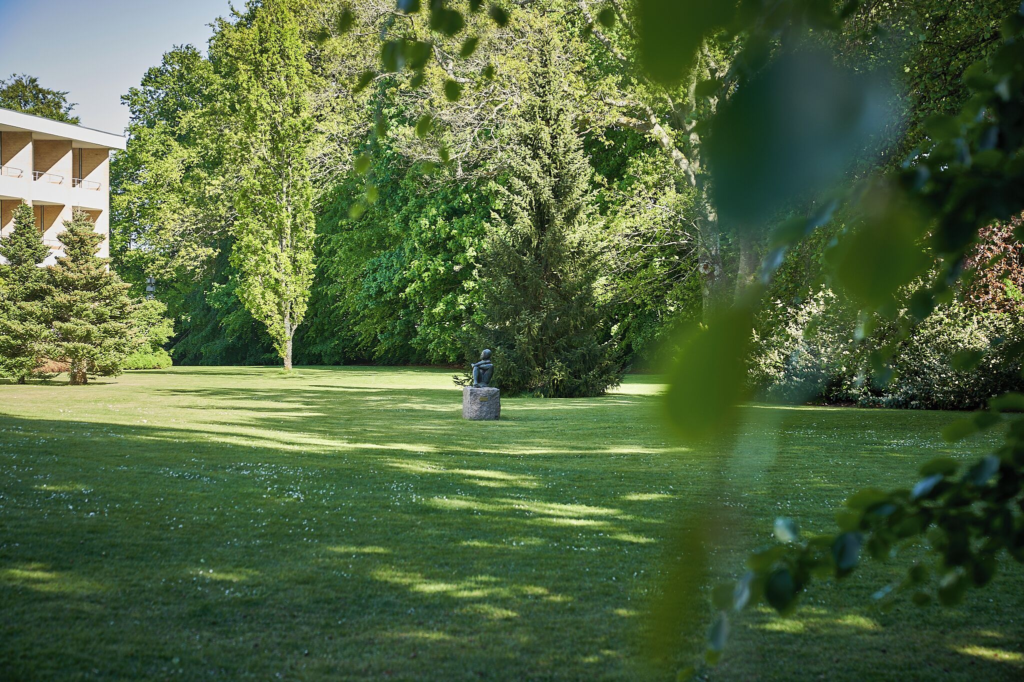 A park with a statue, trees, and a building in the background.