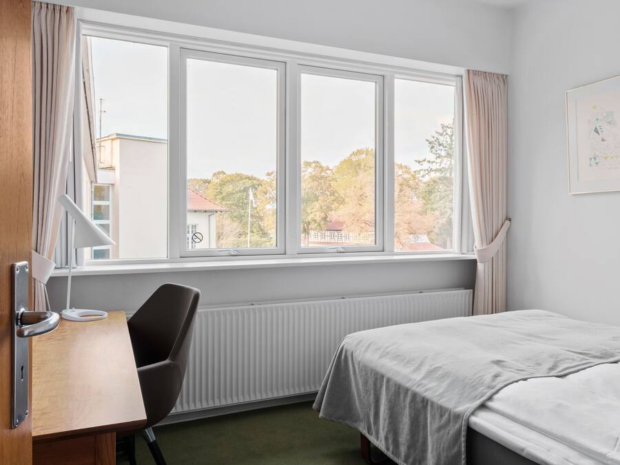 A room with a bed, a desk, and a window with curtains.