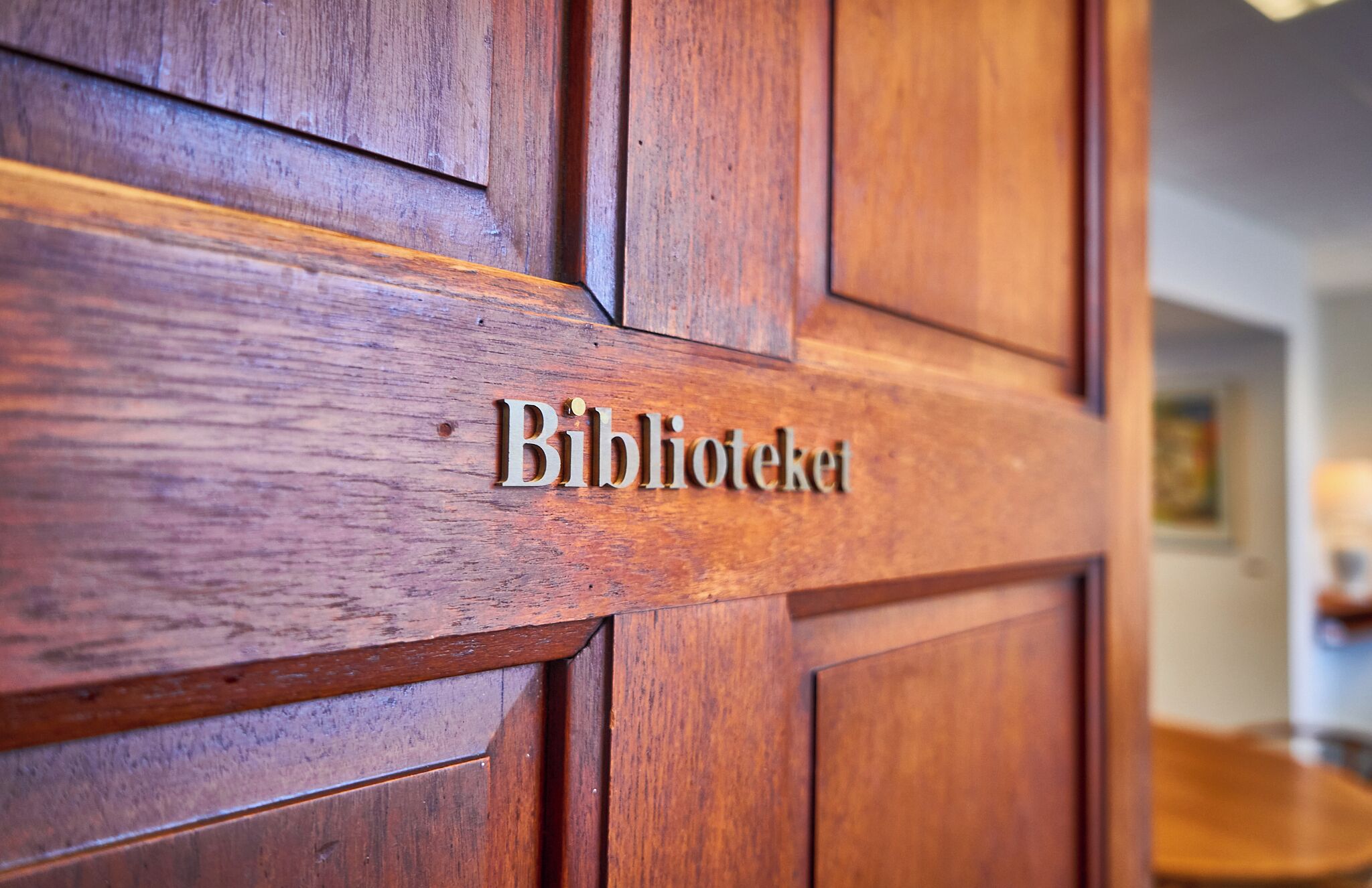 Une porte en bois portant l’inscription « Biblioteket », qui indique la présence d’une bibliothèque ou d’une salle de lecture.