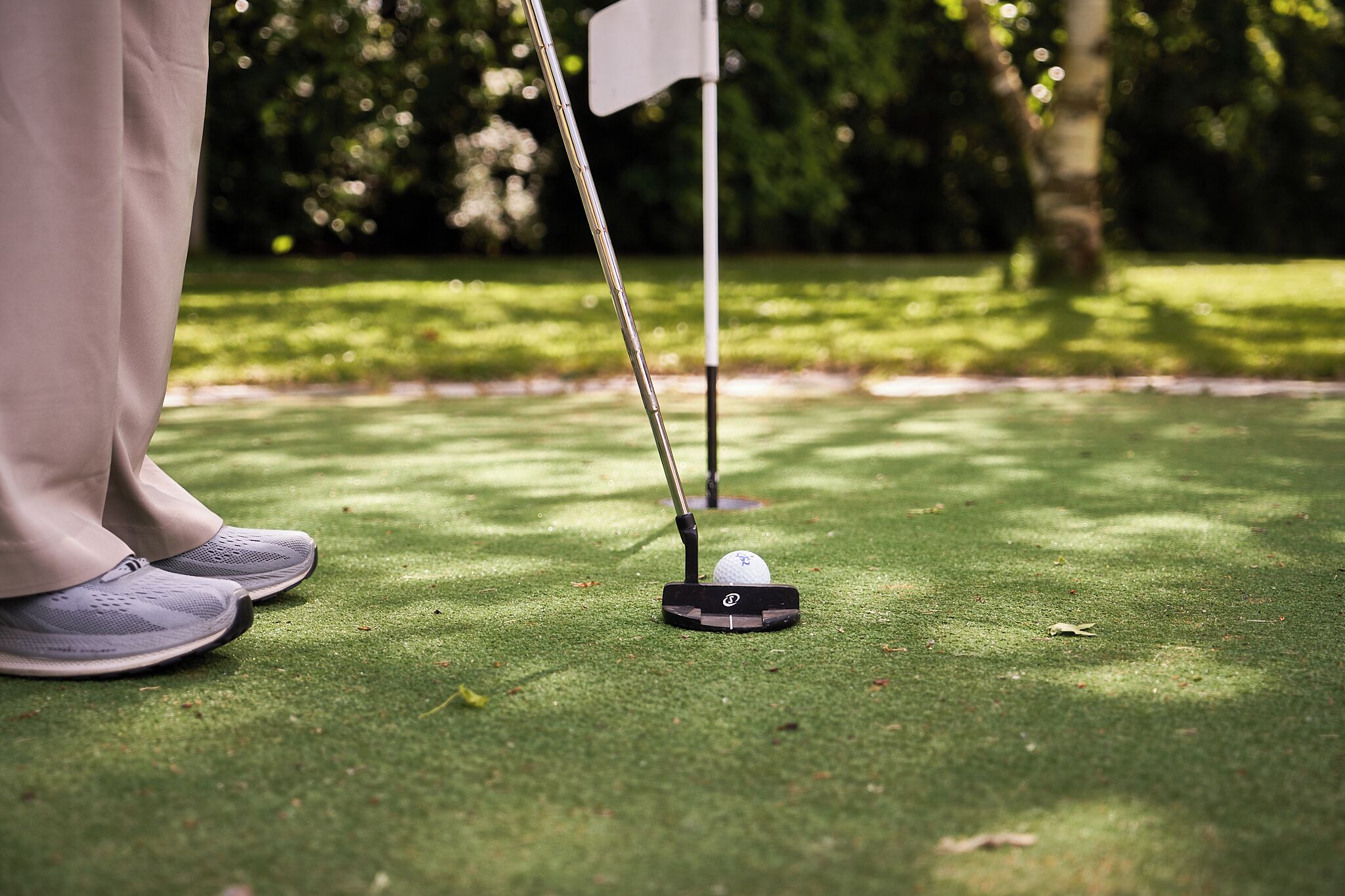 A close-up of a golf club's head on a green, with a flagstick in the background.