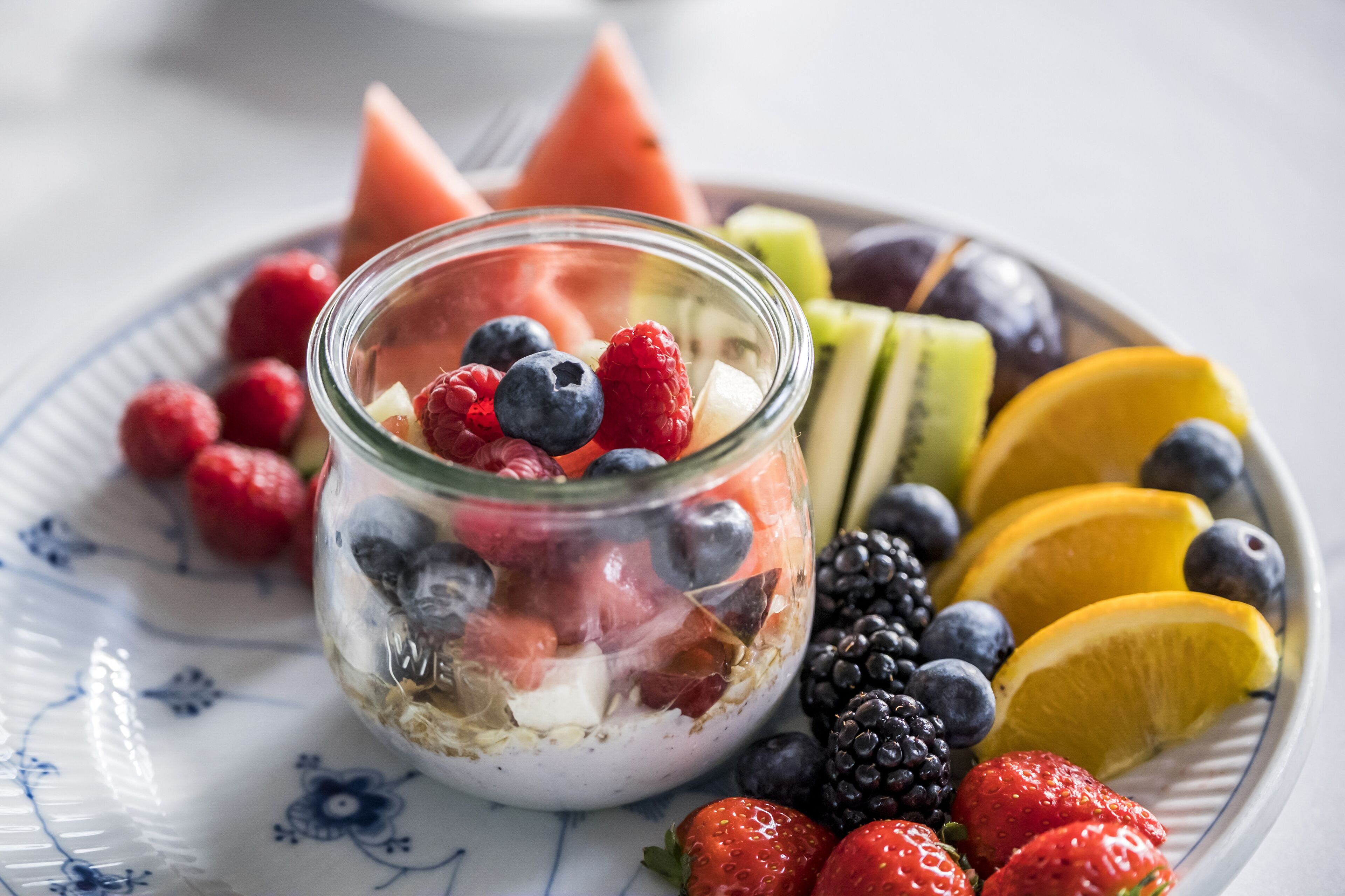 Et glas fyldt med yoghurt og blandede bær, omgivet af frugtskiver på en tallerken.