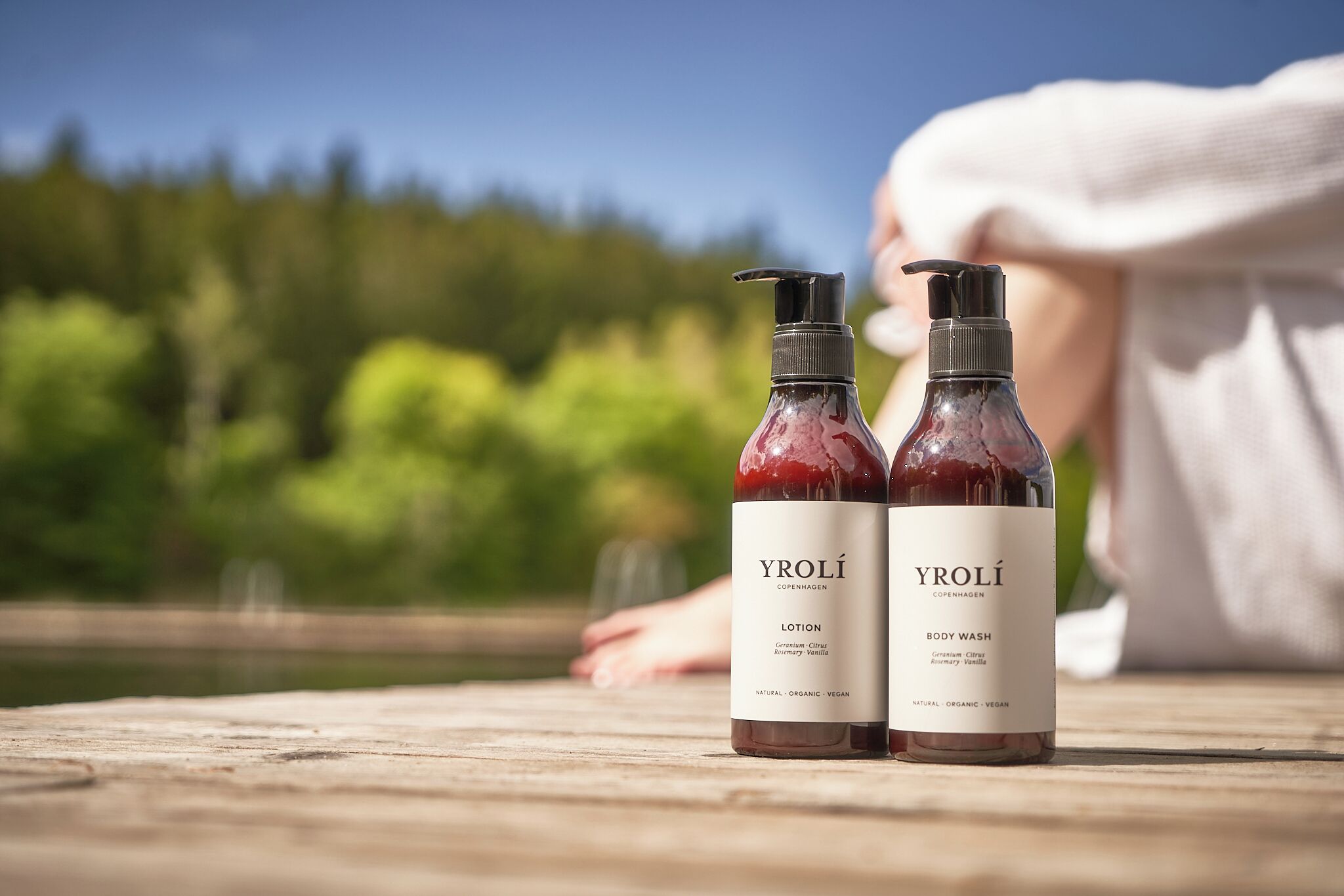 Two bottles of Yrolí body wash on a wooden surface with a blurred natural background.