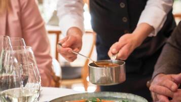 Un camarero sirve comida a los comensales en una mesa con copas de vino y platos.