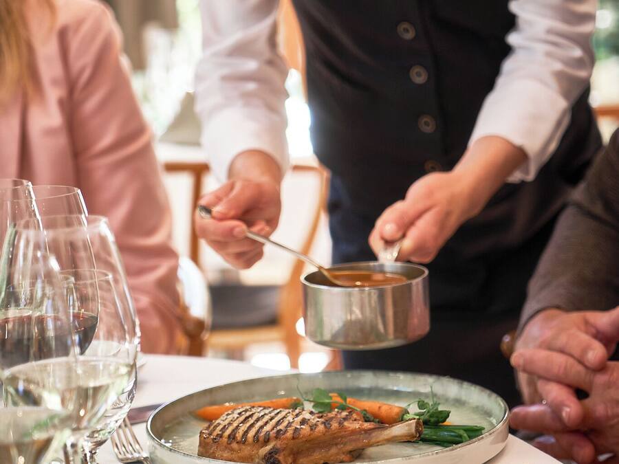 Un camarero sirve comida a los comensales en una mesa con copas de vino y platos.