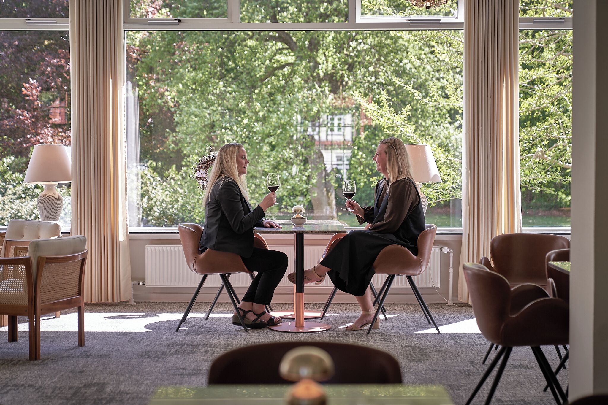 Two people seated at a table with a view of trees through large windows.