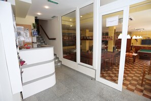 A hotel lobby with a reception desk, a staircase, and a pool table area.