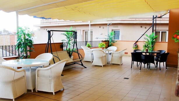 A covered outdoor patio with wicker furniture, potted plants, and a swing set. - Royal Inn Aparthotel (Lloret de Mar)