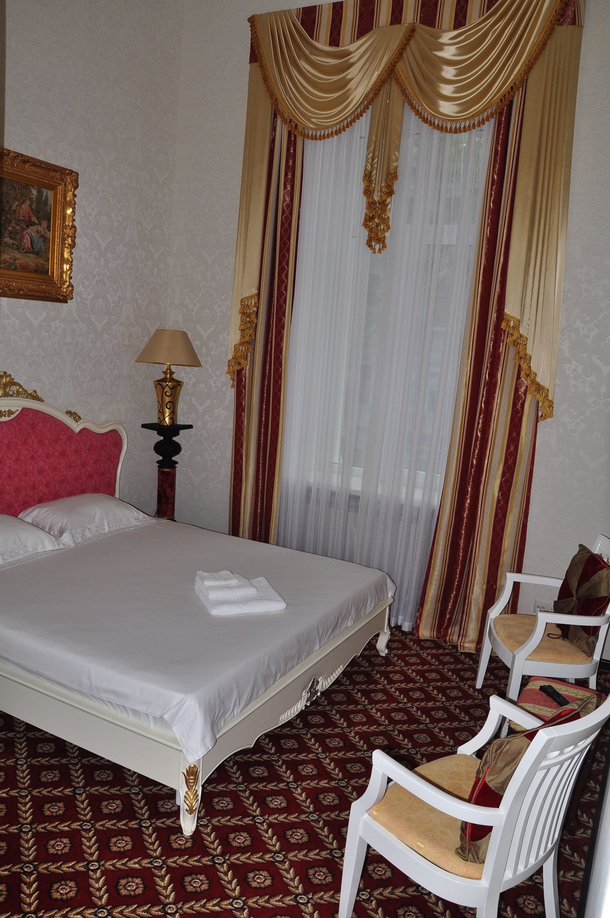 Una camera d'albergo con un letto grande, una sedia, una lampada e un quadro appeso al muro.